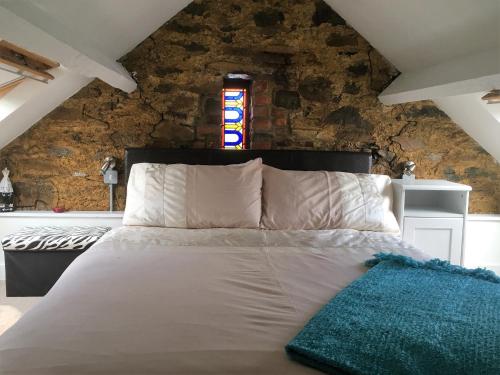 1 dormitorio con cama blanca y pared de piedra en The Barn at Pink Cottage, en Crossgar