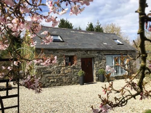 um chalé de pedra com uma porta vermelha e flores cor-de-rosa em The Barn at Pink Cottage em Crossgar