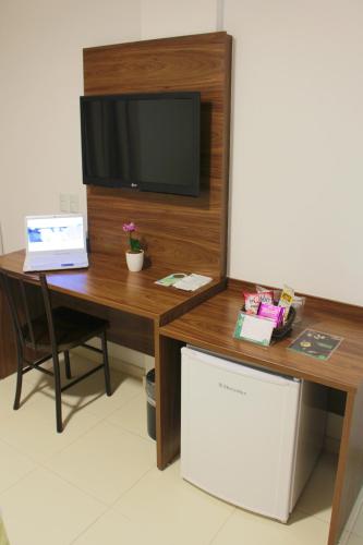 a desk with a television and a table with a refrigerator at Hotel Jardins in Serra