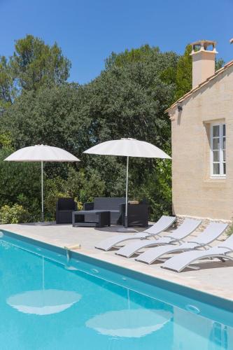 two umbrellas and lounge chairs next to a swimming pool at Le Mas des Alexandrins in Uzès