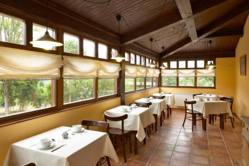 un restaurante con mesas y sillas blancas y ventanas en Hotel Rural Coviella, en Coviella