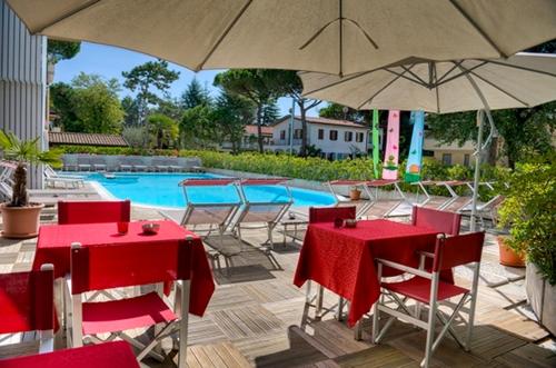 un gruppo di tavoli e sedie con ombrelloni accanto alla piscina di Hotel Friuli a Lignano Sabbiadoro
