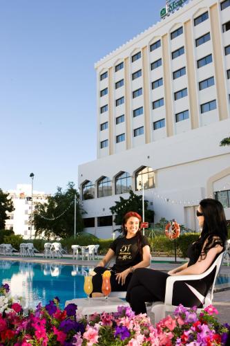 two women sitting in chairs in front of a pool at Hotel Muscat Holiday in Muscat