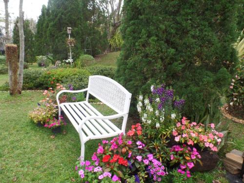 a white bench in a garden with flowers at Baan JaoKorKluay บ้านเจ้ากอกล้วย in Chiang Rai