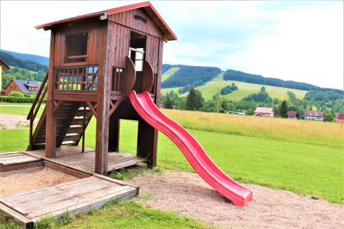 a wooden playground with a red slide in a field at Pension Kohler in Deštné v Orlických horách