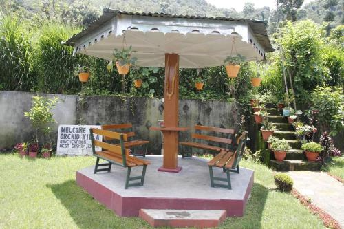 two benches sitting under an umbrella in a garden at Vamoose Orchid Villa Homestay in Rinchingpong