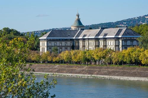a large building next to a river with trees at Ensana Grand Margaret Island in Budapest