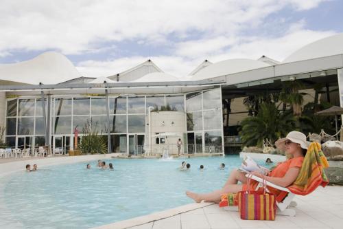 une femme assise sur une chaise en face d'une piscine dans l'établissement Résidence Pierre & Vacances Les Rives de la Seugne, à Jonzac