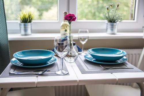 a table with plates and glasses and a vase with a flower at apartamenty Orla in Międzyzdroje