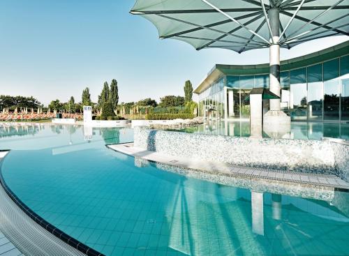 a swimming pool with an umbrella next to a building at Therme Laa Hotel Silent Spa Villas in Laa an der Thaya