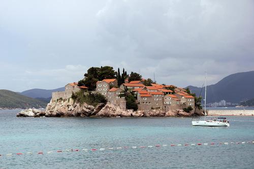 a small boat in the water in front of an island at Royal Holiday Apartments Sveti Stefan in Sveti Stefan