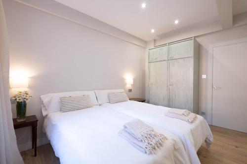 a white bedroom with a large white bed with two pillows at Apartamento Tiboli con parking gratuito in Bilbao