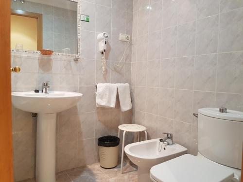een badkamer met een wastafel, een toilet en een spiegel bij Hotel Camargo in Igollo