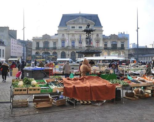 a market with fruits and vegetables on tables in front of a building at Chez MARLENE in Quettehou
