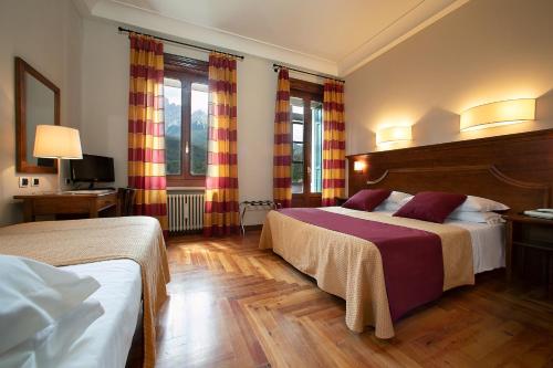 una camera d'albergo con due letti e due finestre di TH Borca di Cadore - Park Hotel Des Dolomites a Borca di Cadore