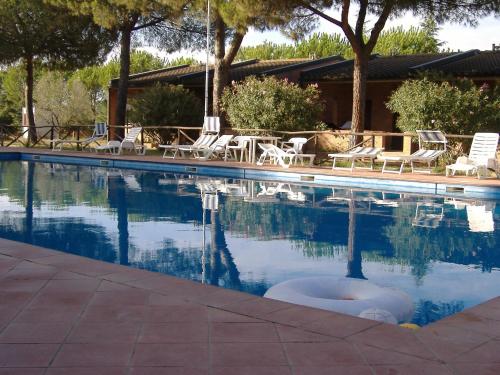 a swimming pool with chairs and trees and a house at Baia Etrusca Resort in Riotorto