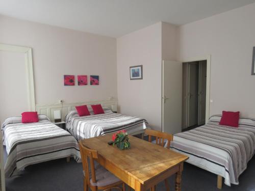 a room with three beds and a wooden table at Hotel Richelieu in Eaux-Bonnes