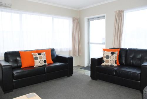 a living room with two black leather couches and orange pillows at Almond Court Motel in Alexandra