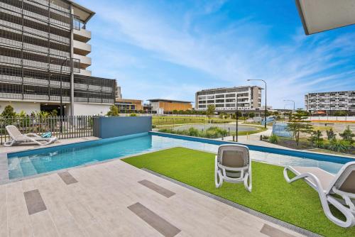a swimming pool with two chairs and a grassy area at Aquarius Kawana in Kawana Waters