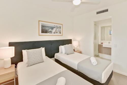 a white bedroom with two beds and a lamp at Aquarius Kawana in Kawana Waters