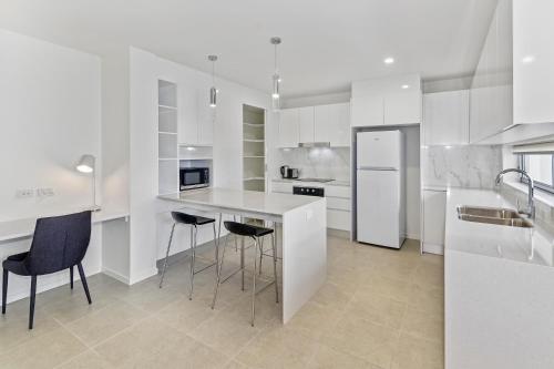 a white kitchen with a counter and stools at Aquarius Kawana in Kawana Waters