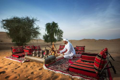 a man sitting next to a fire in the desert at Telal Resort Al Ain in Al Ain