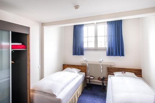 two beds in a small room with blue curtains at Boutique-Hotel Rüden in Schaffhausen