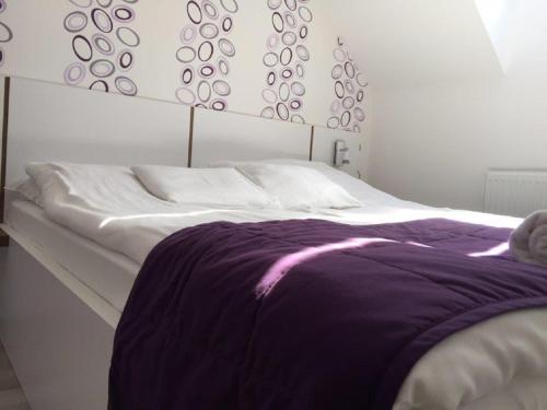 Una cama blanca con una manta morada. en ALOE Apartman, en Sárvár