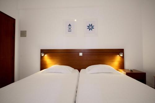 two beds in a hotel room with white sheets at Hospedaria Buganvilia Alvor in Alvor