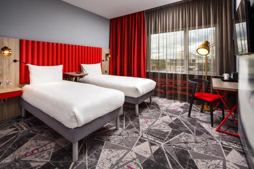 two beds in a hotel room with red curtains at ibis Styles London Ealing in London