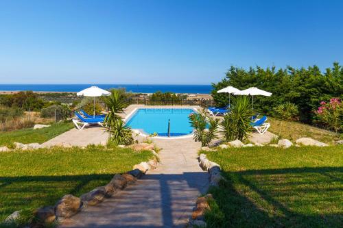 a swimming pool with chairs and umbrellas and the ocean at Villa Alexi in Kalathos