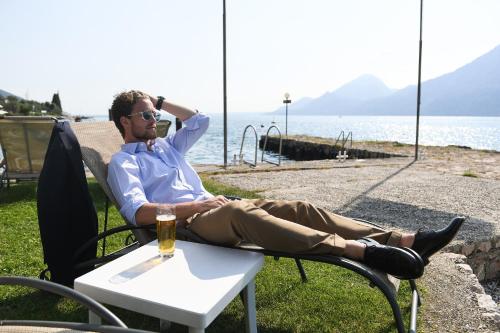 a man sitting in a chair with a glass of beer at Hotel Du Lac - Relax Attitude Hotel in Brenzone sul Garda