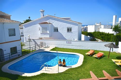 dos personas sentadas junto a una piscina en un patio en Apartamentos Luna de Nerja, en Nerja