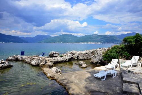 two white chairs sitting on the edge of a body of water at Apartmani M&E in Tivat