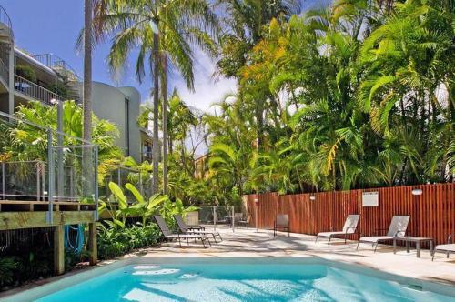 a swimming pool with chairs and a fence and palm trees at Naousa II in Noosa Heads