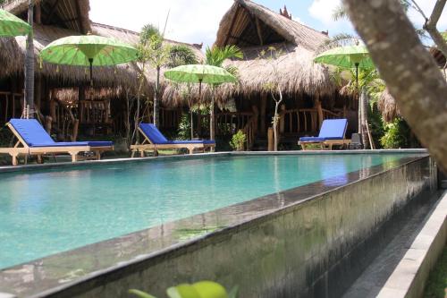 a swimming pool at a resort with chairs and umbrellas at The Calmtree Bungalows in Canggu