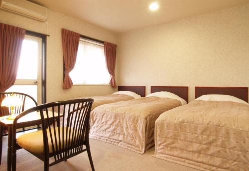 1 dormitorio con 2 camas, mesa y ventana en Akakura Yours Inn en Myoko