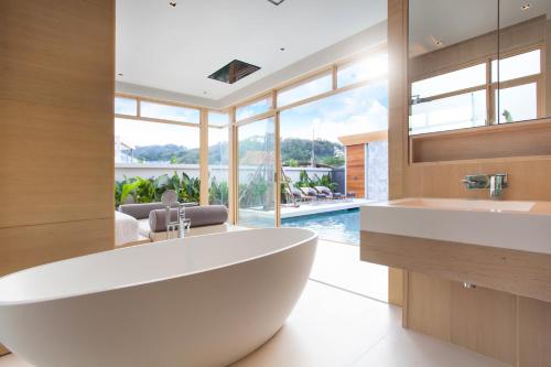 a large white tub in a bathroom with a pool at Himmapana Villas - SHA Extra Plus in Kamala Beach