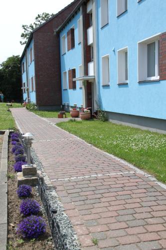 a brick path next to a blue building with purple flowers at Haus Marinus in Puttgarden