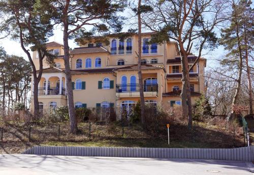 a large yellow building with blue windows and trees at Baabe Grüne Düne Fewo Sommerfrische - 13 (Ref.199157) in Baabe