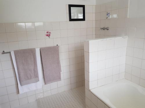 a white tiled bathroom with a bath tub and towels at Norfolkden Beachhouse in Hermanus