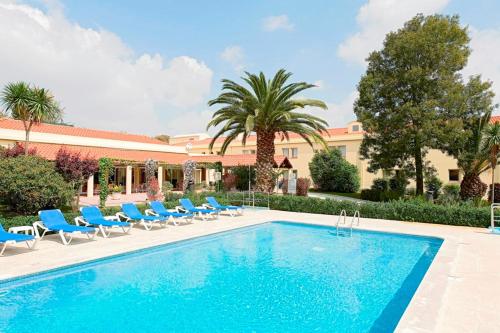 a swimming pool with blue chairs and a building at Hotel ibis Setubal in Setúbal