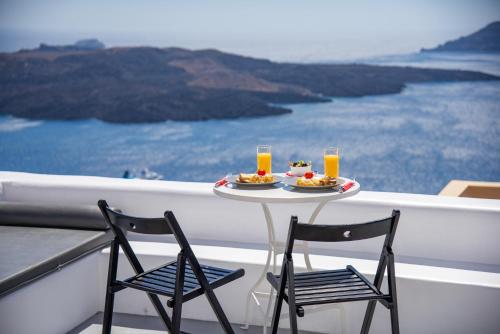 a table with two chairs and two glasses of orange juice at NK Cave House Villa in Fira