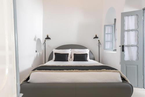 a white bedroom with a large bed with two black pillows at NK Cave House Villa in Fira