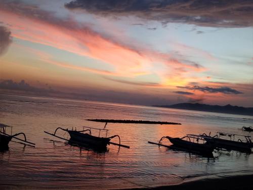 three boats sitting in the water at sunset at Puri Oka Beach Bungalows in Candidasa