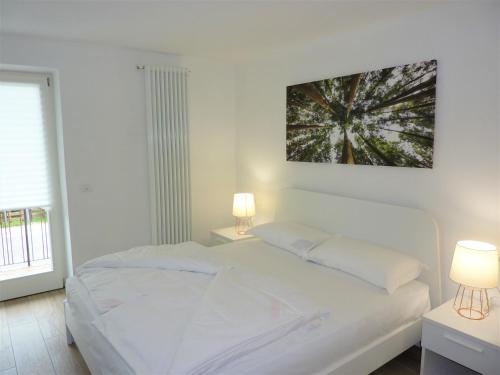 a white bedroom with a white bed and two lamps at Trentino Apartments - Casa ai Tolleri in Folgaria