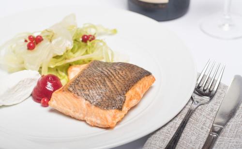 a white plate with a piece of fish and a salad at Hotel Viest in Vicenza