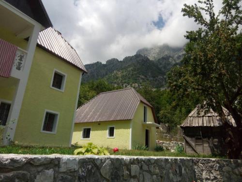a yellow house and a building with mountains in the background at Bujtina Ahmetaj in Valbonë
