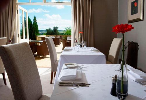 a dining room with two tables and a red flower in a vase at Loch Ness Country House Hotel in Inverness