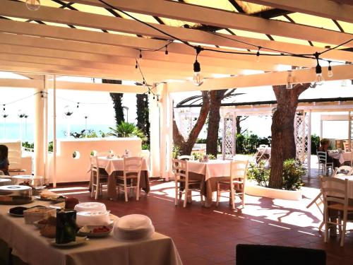 een restaurant met witte tafels, stoelen en ramen bij Hotel Residence La Corvetta in Monopoli